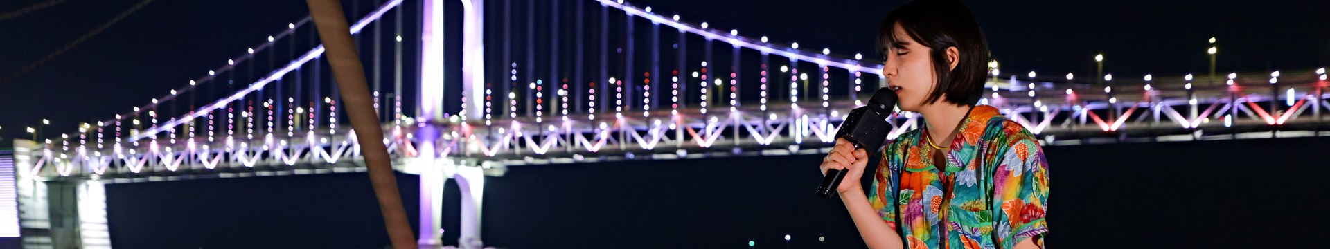 広安大橋を背景に、ヨットの船首で歌うバスキングのアーティスト